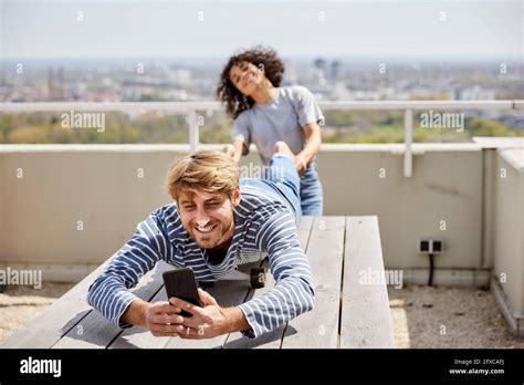 Man Using Mobile Phone While Girlfriend Pulling Leg On Terrace Stock