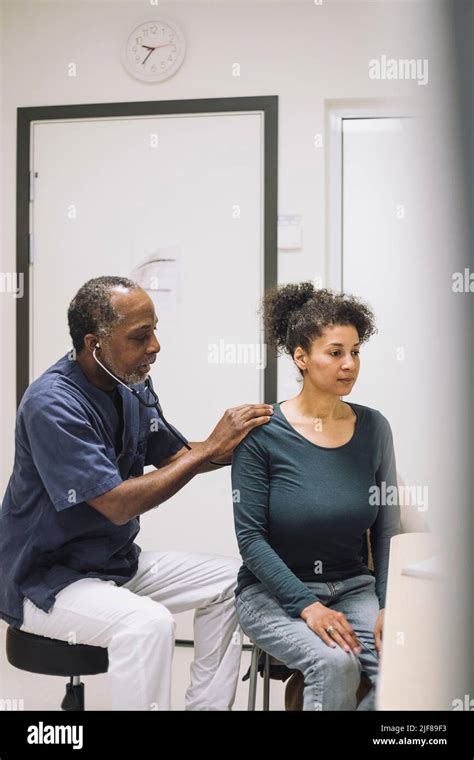 Male Doctor Examining Female Patient With Stethoscope In Medical Clinic