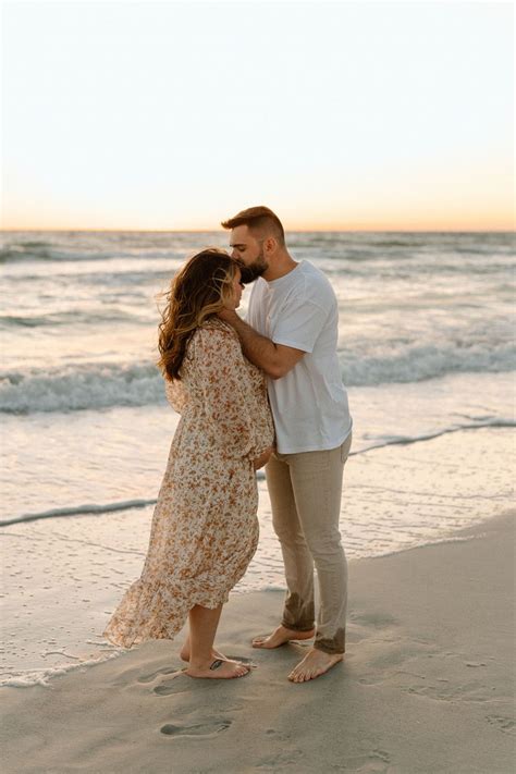 an engaged couple kissing on the beach at sunset