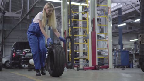 Young Caucasian woman rolling tire in repair shop. Smiling female auto ...