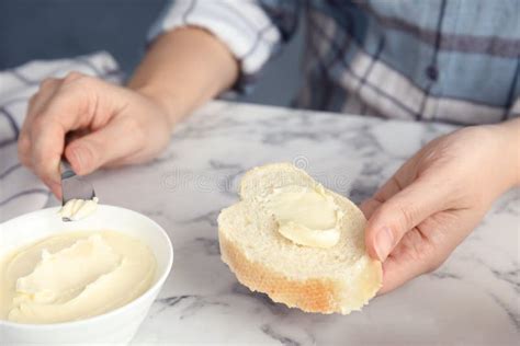 Woman Spreading Butter Onto Slice Of Bread Over Marble Table Stock