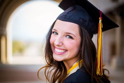 a woman wearing a graduation cap and gown smiling at the camera with an arch in the background