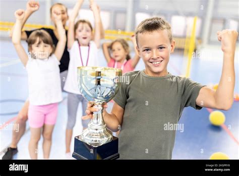 Happy Boy Flexing Muscle Holding Trophy With Friends At School Sports