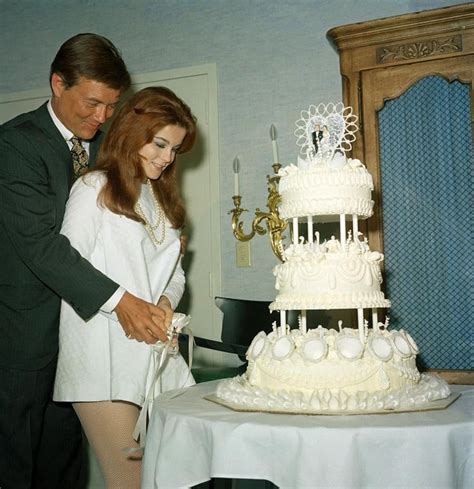 A Man And Woman Are Cutting Into A Wedding Cake With White Frosting On It