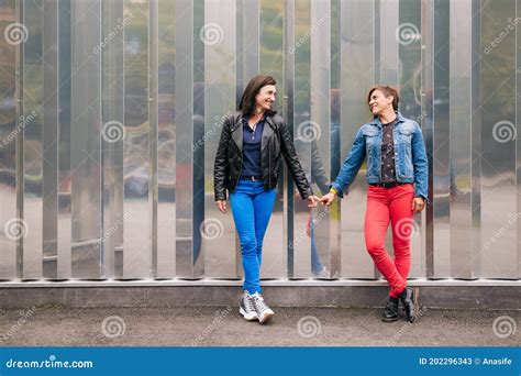 Happy Middle Aged Lesbian Couple Holding Hands Against A Metallic Wall Stock Image Image Of