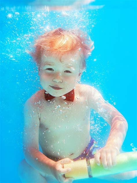 Little Boy Infant With Red Butterfly Diving Underwater In Swimming Pool