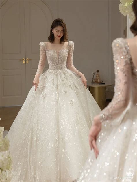 A Woman In A Wedding Dress Standing Next To Another Woman Wearing A Gown With Sequins On It