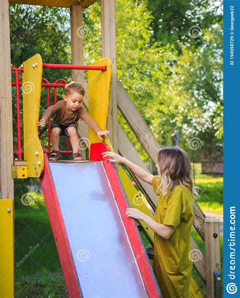 Smiling Baby Boy With Mother Ride On Children`s Slide In Playground In