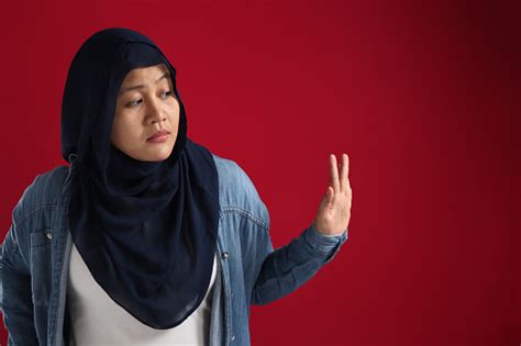 Asian Muslim Woman Wearing Hijab Rejecting Avoiding Something From The Side Red Background With