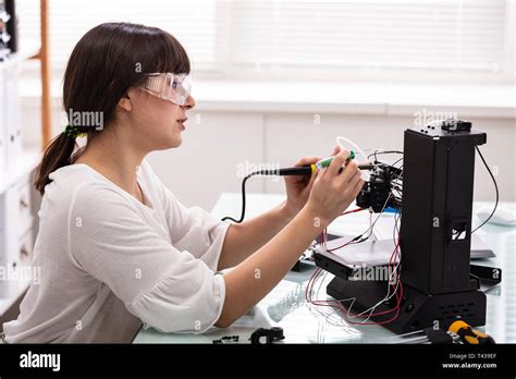 Young Female Technician Wearing Safety Eyeglasses Using Soldering Iron