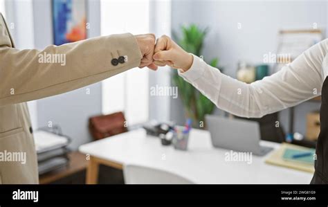 Two Coworkers Performing A Fist Bump In An Office Setting Signifying Teamwork And Partnership