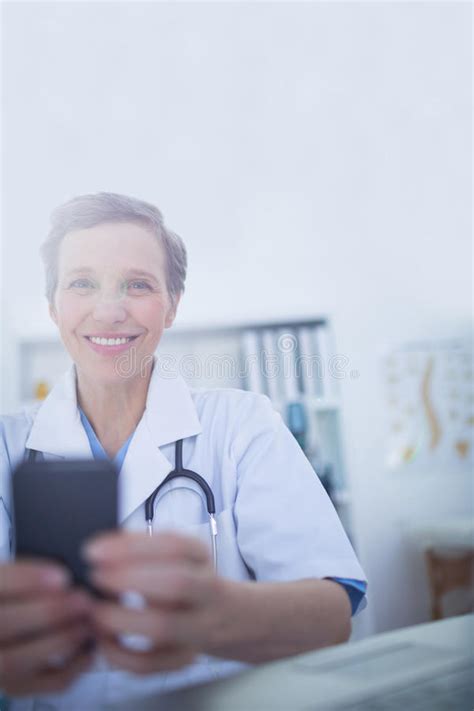Happy Doctor Looking At Camera And Using Her Smartphone Stock Photo