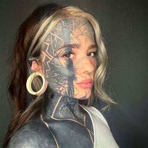 A Woman With Tattoos On Her Face And Body Is Posing For A Photo In Front Of A Black Background