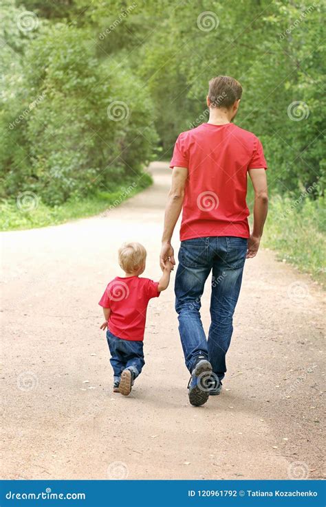 Father And His Toddler Boy Are Walking In The Park Holding Hands
