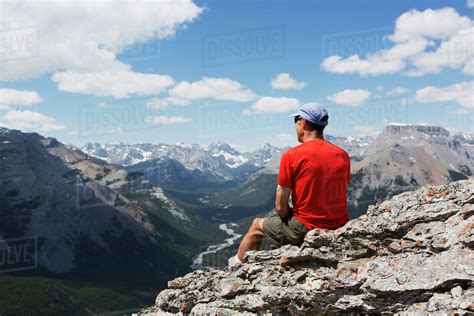 Male Hiker Sitting On A Rocky Cliff Ledge Overlooking A River Valley