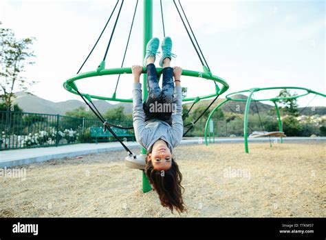 Portrait Of Girl Hanging Upside Down On Outdoor Play Equipment Against