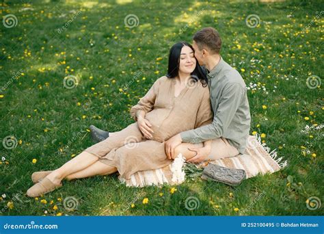 Pregnant Woman And Her Husband Sitting In A Park On A Grass And Hugging Stock Image Image Of