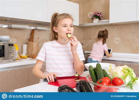 Preteen Girl Cutting And Eating Cucumber With Knife On A Table In