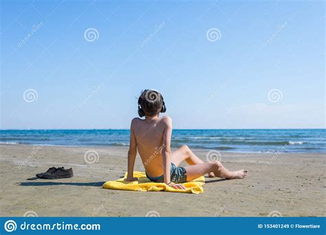 Teen Boy Is Sitting On Yellow Towel In The Headphones And Sunbathes On