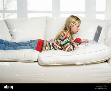 Young Girl Lying On Stomach On Sofa Using Laptop Side View Stock