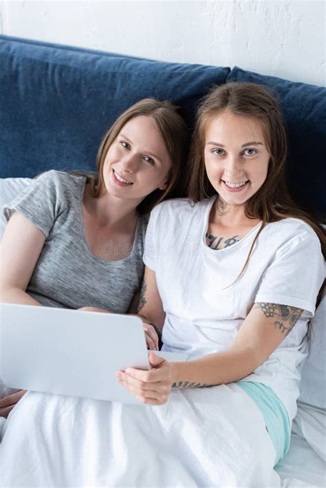 Two Smiling Lesbians Looking At Each Other While Using Laptop In Bed In Morning Stock Image