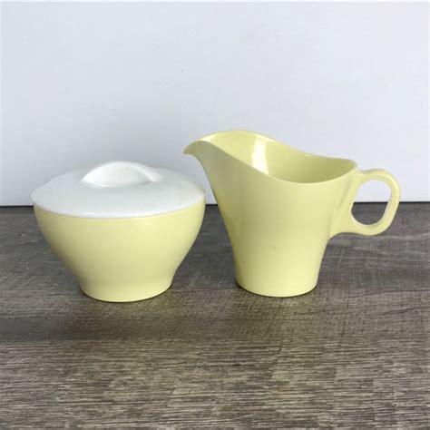Two Yellow And White Pitchers Sitting On Top Of A Wooden Table Next To Each Other