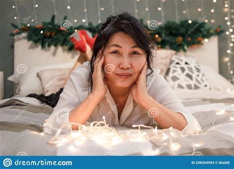 Senior Asian Woman Relax On Bed With Xmas Lights Charming Elderly Smiling Lady In Bedroom At