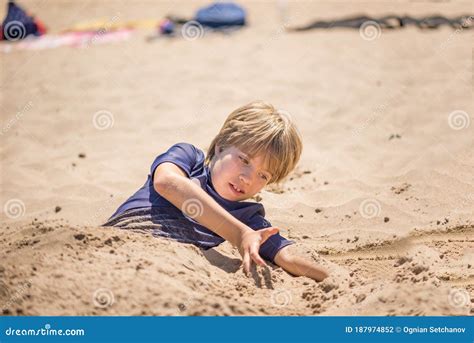Portrait Of A Boy Playing On The Beach Buried In The Sand Stock Photo