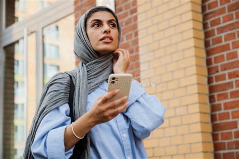 pensive muslim woman wearing hijab using smartphone while standing outdoors stock image image
