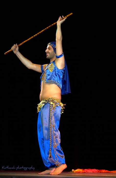 A Man In Blue And Gold Costume Holding A Bamboo Stick Up To His Head