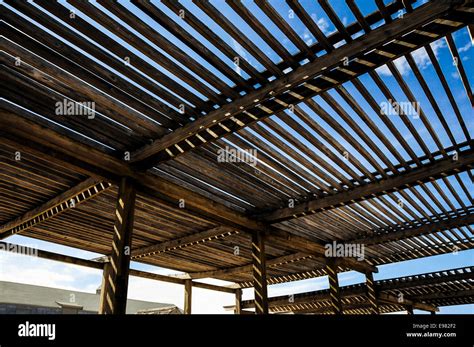 Large Wooden Slat Roof Over A Patio Area With Sunlight And Blue Sky