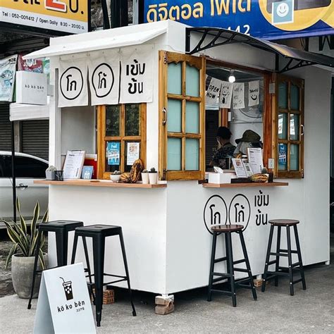 An Outdoor Food Stand With Three Stools And A Sign On The Wall That
