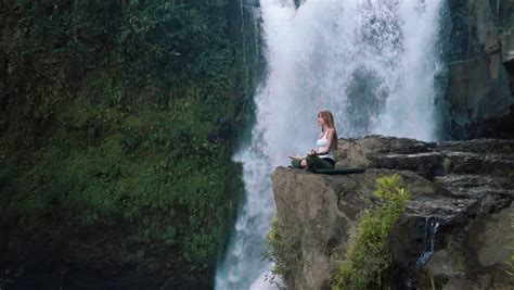 Woman Sitting In Meditation Under Waterfall In Bali Indonesia Stock