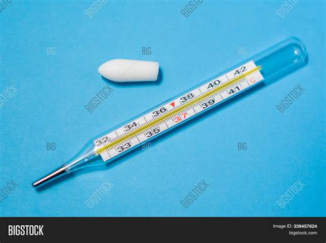 White Suppository For Anal Or Vaginal Use On Blue Background And A Thermometer With Temperature