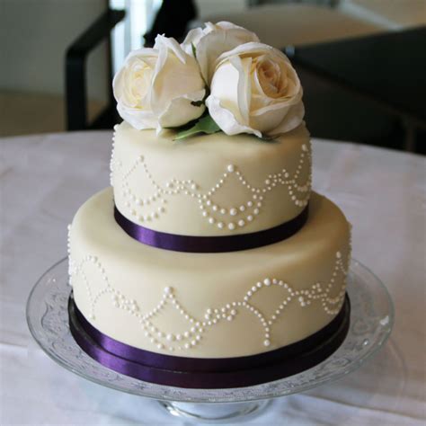 Elegant and simple two tiered cake covered in white royal icing with pink decorative flowers and surrounded by delicious small cupcakes with white buttercream frosting and pink butterfly sugar details. Wedding Gallery | Purple wedding cakes, Wedding cakes ...