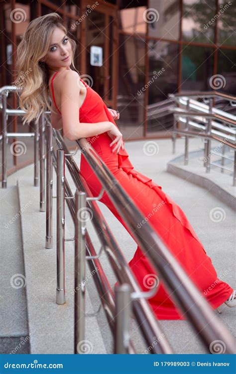 An Elegant Woman In A Tight Red Dress Poses Leaning Against The Railing Of A Street Staircase In