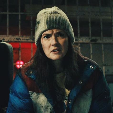 A Woman Wearing A Beanie And Jacket In A Jail Cell With Bars Behind Her