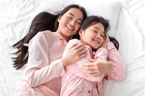 satisfied japanese millennial woman hugging teen girl in pajama lie on bed and have fun in