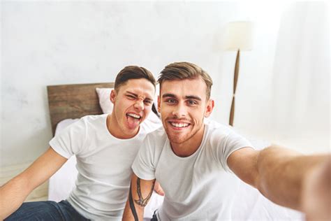 Cheerful Homosexual Couple Making Selfie In Bedroom 2人のストックフォトや画像を多数ご