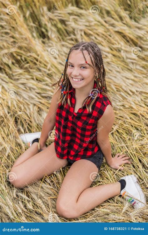 Smiling Teenage Girl With Braids Sitting In Wheat Field At Summer Stock