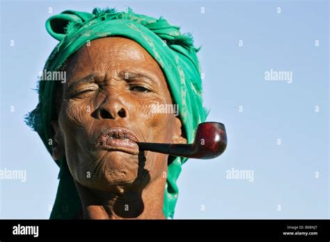 Old Wrinkly Faced Wizened Namibian Woman Smoking A Pipe And Wearing A