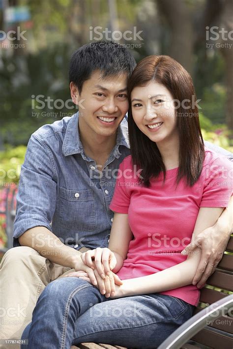 Young Chinese Couple Relaxing On Park Bench Together Stock Photo