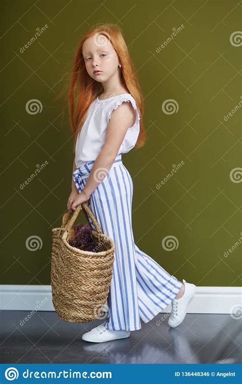Little Red Haired Girl With A Basket Of Flowers Posing On An Olive