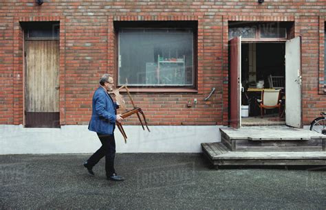 Full length of senior man carrying wooden chair while walking by ...