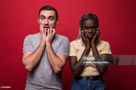 ショック異人種間の肖像 アフリカの女性と白人の男が赤の背景に対して一緒に立って顔を覆い怖がって失望した表現でカメラを見て ウクライナのストックフォトや画像を多数ご用意 Istock