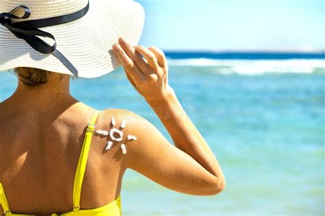 Back View Of Young Woman Tanning At The Beach With Sunscreen Cream In Sun Shape On Her Shoulder