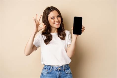 Premium Photo Smiling Happy Girl Showing Mobile Phone Screen App On Smartphone And Okay