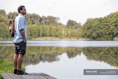 Young Man Standing On A Jetty At Lake Looking At Distance
