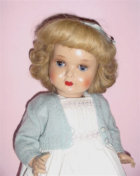 a doll with blonde hair and blue eyes wearing a white dress on a pink background