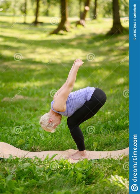 A Middle Aged Woman Practices Yoga Outdoors In A Standing Forward